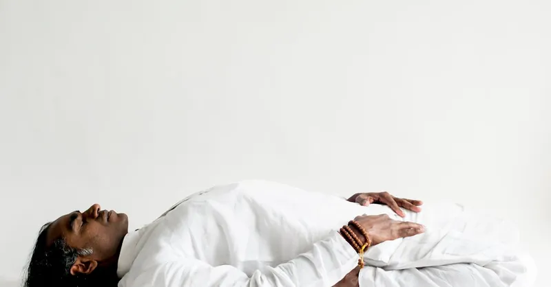 A person in a white outfit practicing meditation, lying down peacefully indoors.