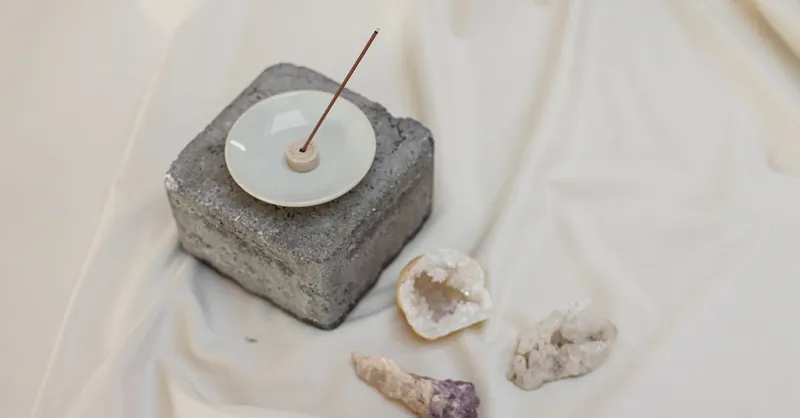 A minimalist setup with an incense stick in a holder and crystals on white linen, offering a sense of inner peace.