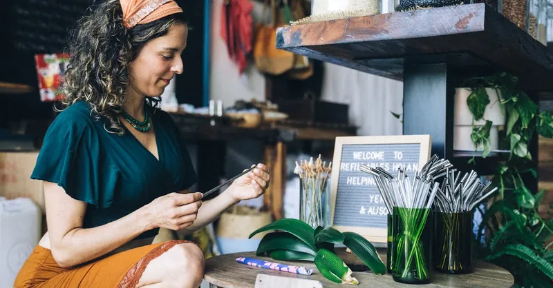 Woman in store with reusable straws and eco-friendly products promoting sustainability.