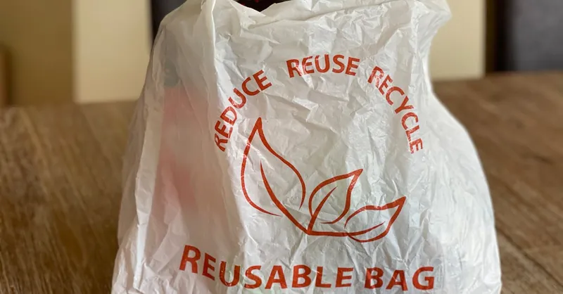 Reusable bag promoting reduce, reuse, recycle on a wooden table indoors.