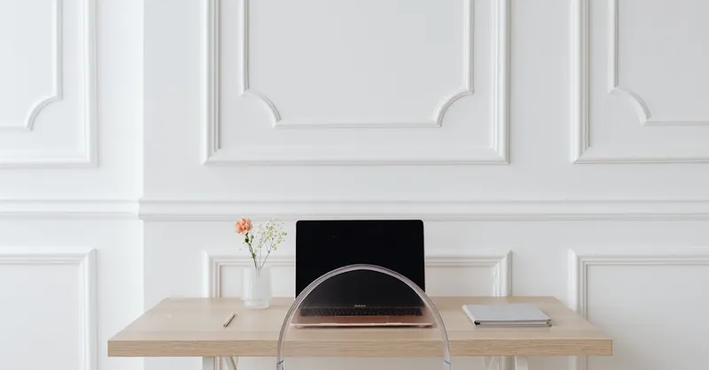 Elegant minimalist office setting with laptop, notebook, and decor on a wooden desk.