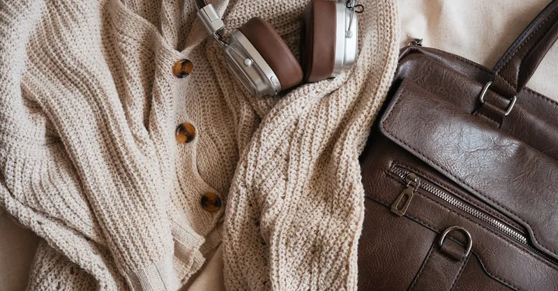 Warm fashion flat lay with knit cardigan, headphones, and leather bag.