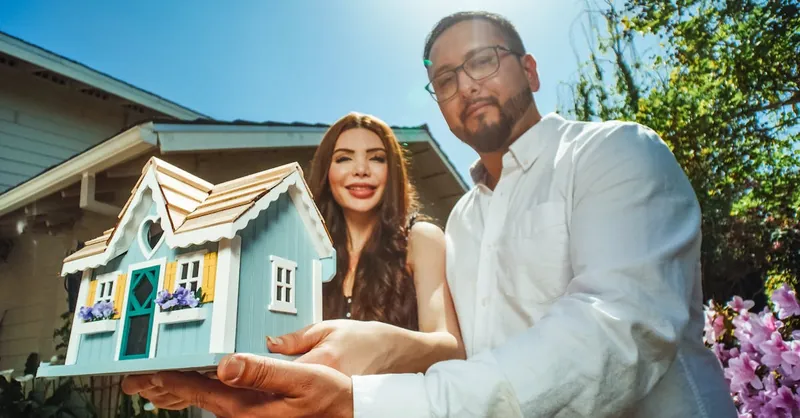Happy couple proudly holding a miniature house symbolizing new homeownership.