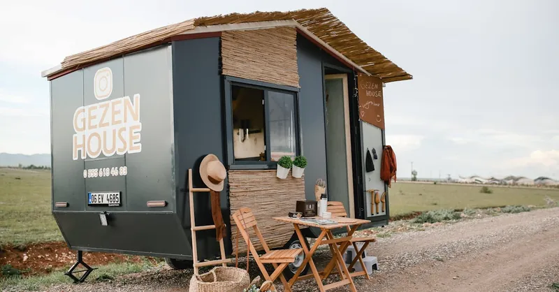 Mobile tiny house with outdoor furniture on a countryside dirt road.